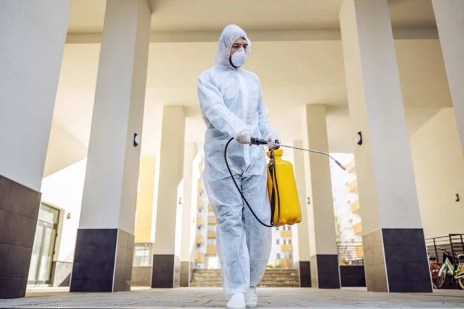 Un hombre con traje de protección y máscara está rociando un edificio con un pulverizador.