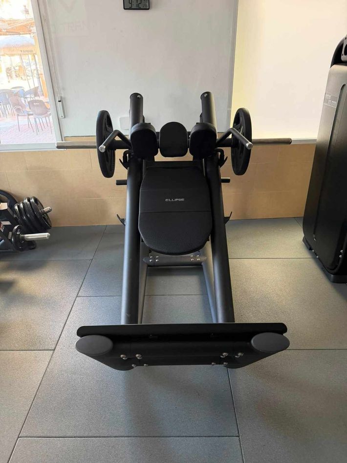 Máquina de ejercicios negra en un gimnasio, centrada sobre un suelo de goma cerca de una ventana.