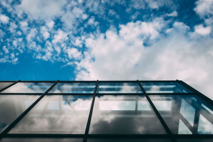 Mirando hacia un techo de cristal con un cielo azul y nubes reflejados en él.