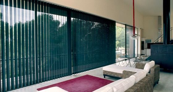 Una sala de estar con un sofá y una alfombra y persianas verticales en las ventanas.