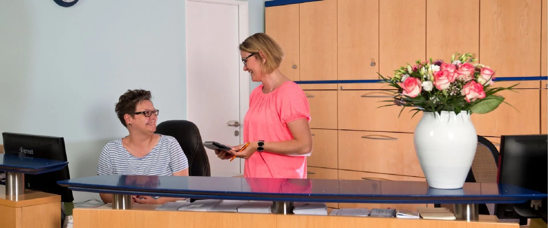 Zwei Frauen stehen an einem Empfangstresen in einem Büro.