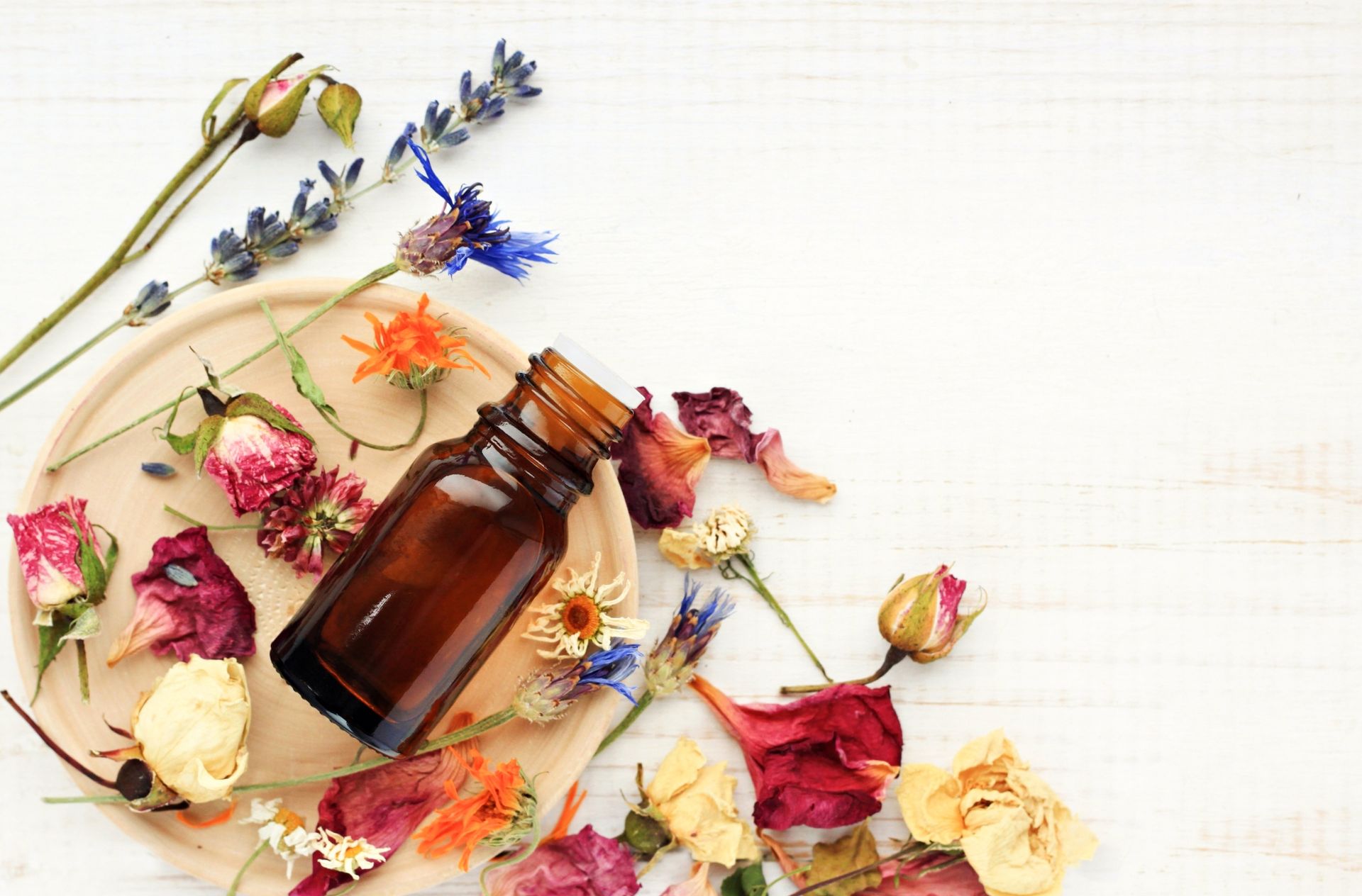 Pétales de fleurs séchées et un flacon d'huile essentielle posés sur un support en bois 