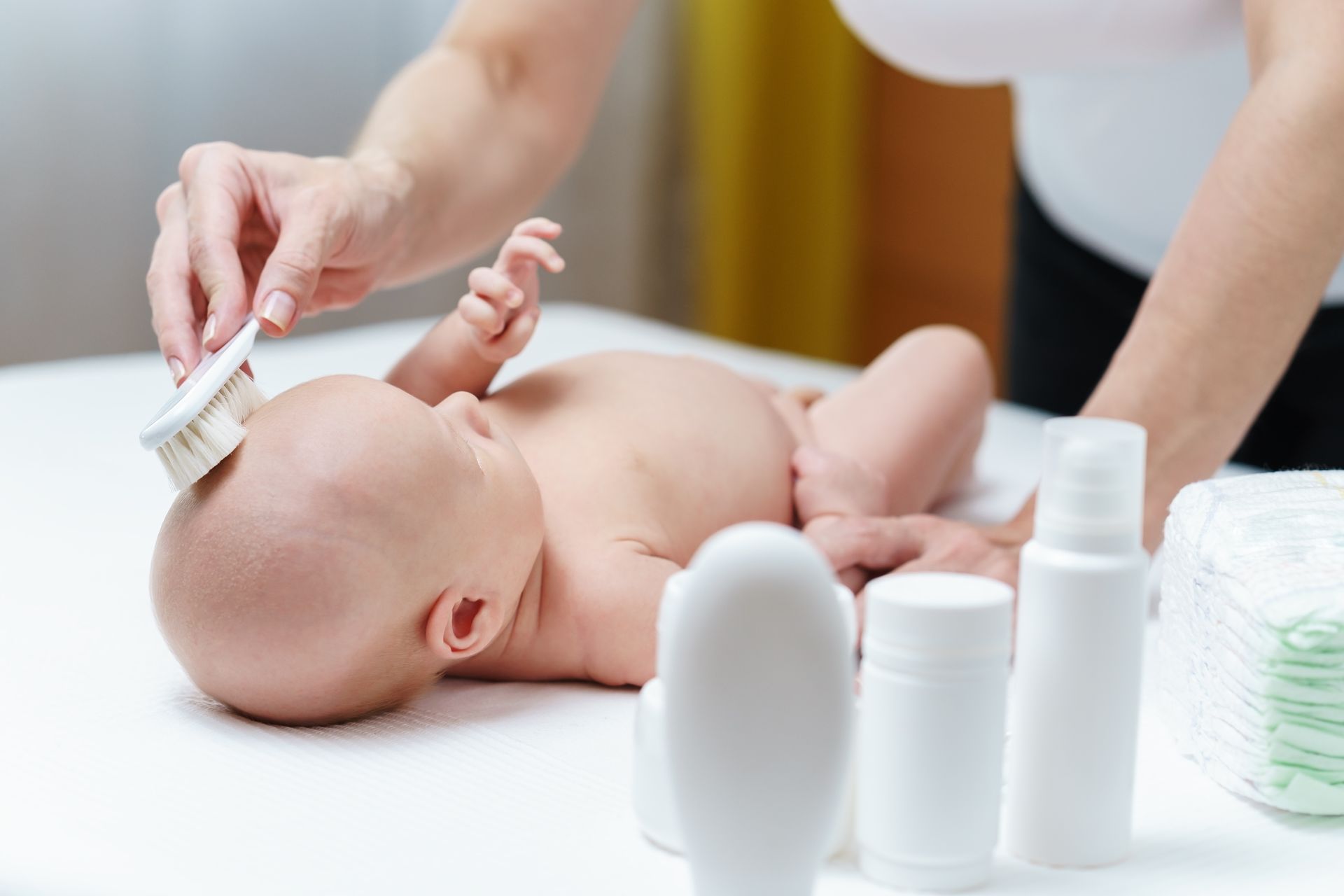 Parent qui fait la toilette de son bébé avec des produits de soin au premier plan