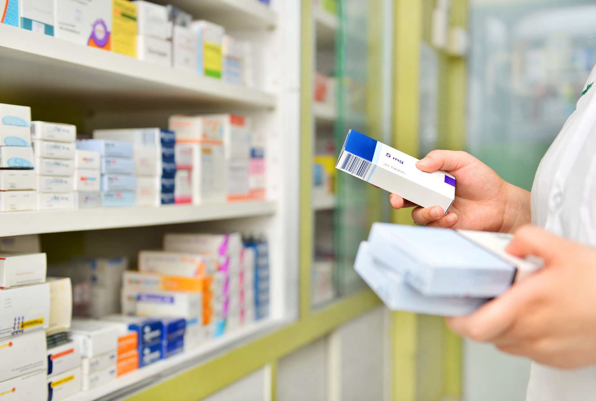 Main qui tient une boîte de médicaments devant un étalage de médicaments