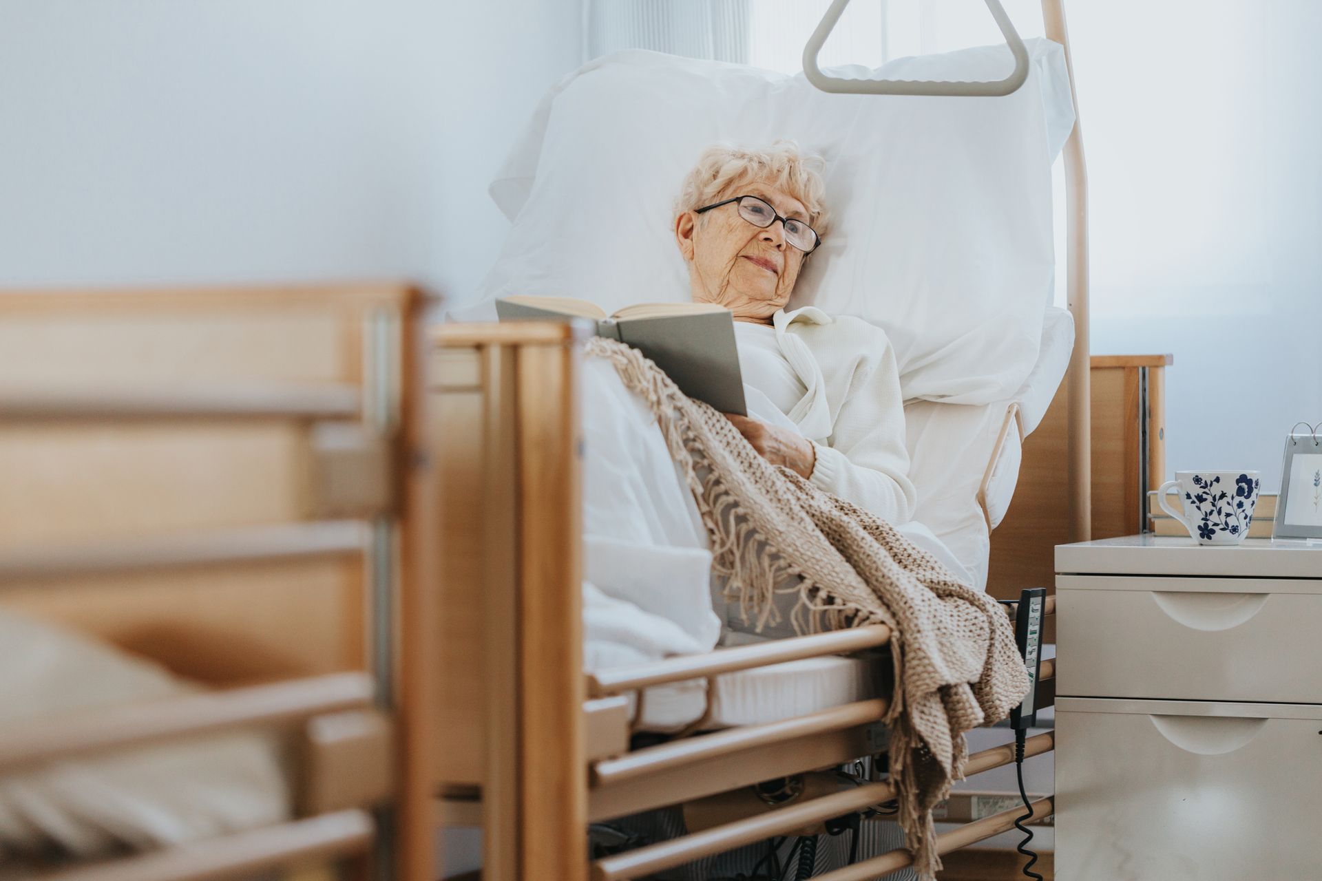 Dame âgée qui lit un livre, allongée sur un lit médicalisé