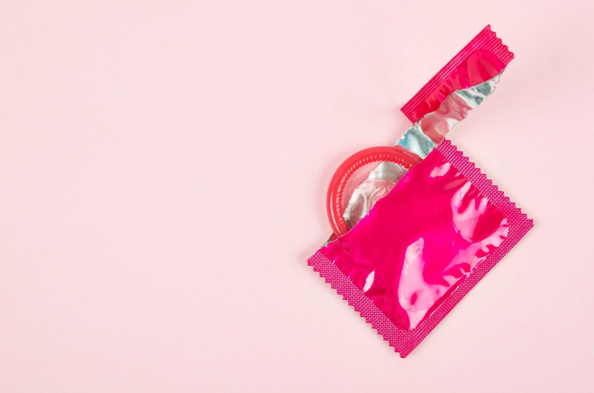 Emballage d'un préservatif rose ouvert et un préservatif rose