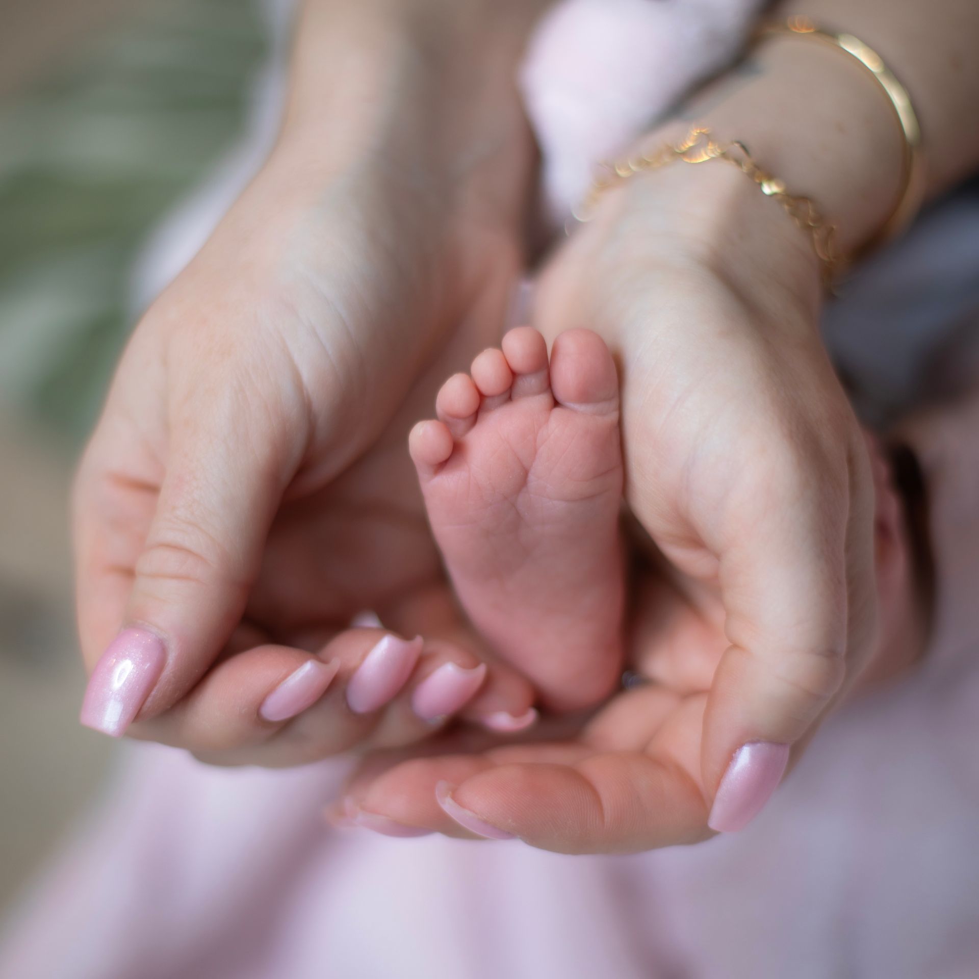 Mains de femme avec du vernis rose qui enveloppent un pied de nourrisson