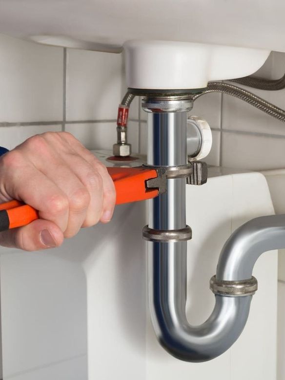 Apretando a mano un tubo de desagüe cromado con una llave naranja debajo de un lavabo.