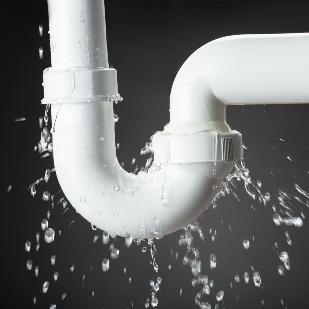 Fuga en una junta de tubería de PVC blanca que rocía agua sobre un fondo oscuro.