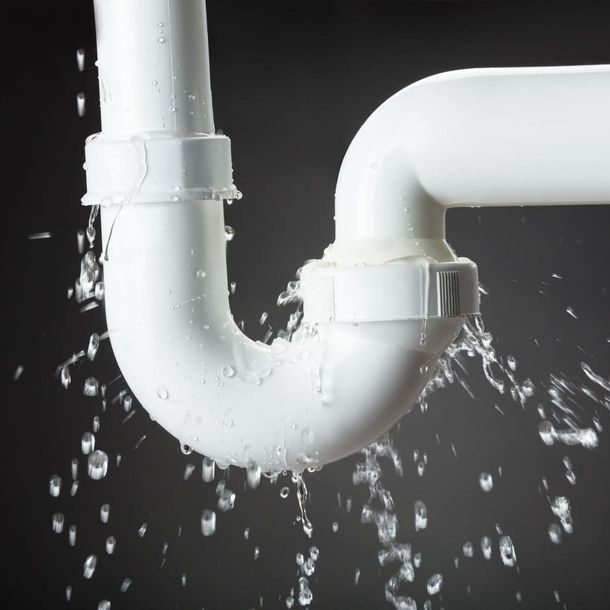Fuga en una junta de tubería de PVC blanca que rocía agua sobre un fondo oscuro.