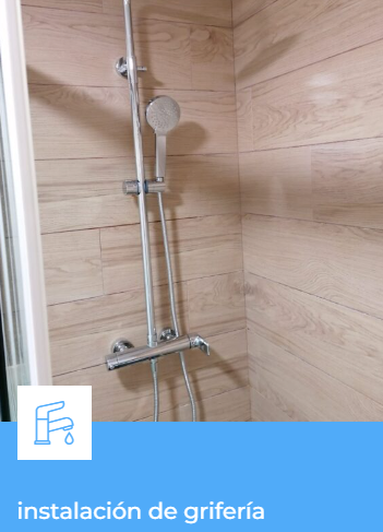Grifo de ducha cromado instalado sobre pared de azulejo beige en un baño.