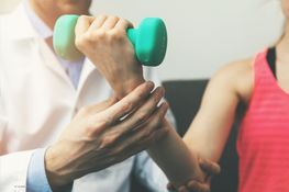 Physiotherapeut unterstützt eine Frau beim Heben einer Hantel