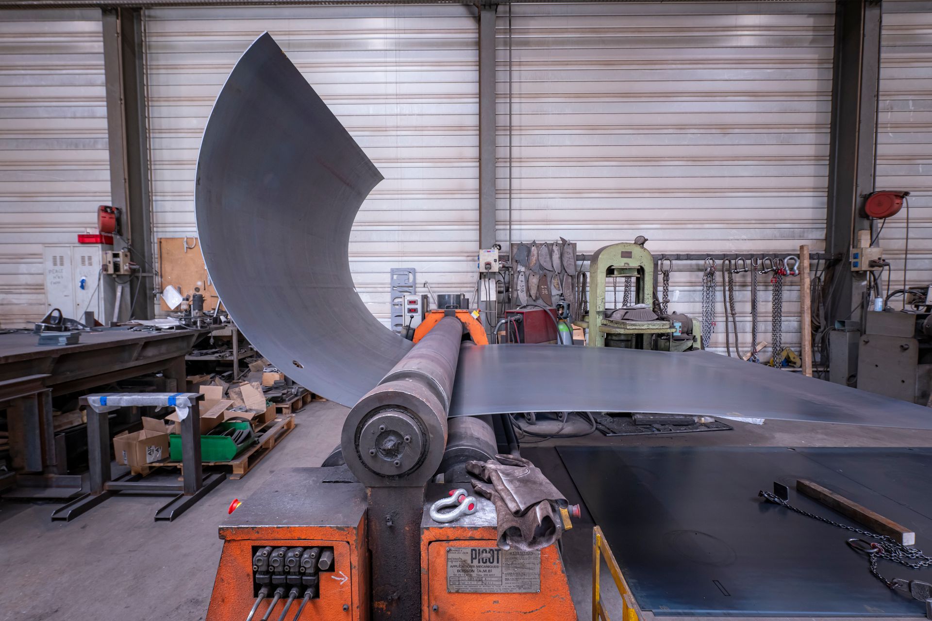 Dans un atelier, une grande machine façonne des tôles en forme courbe.