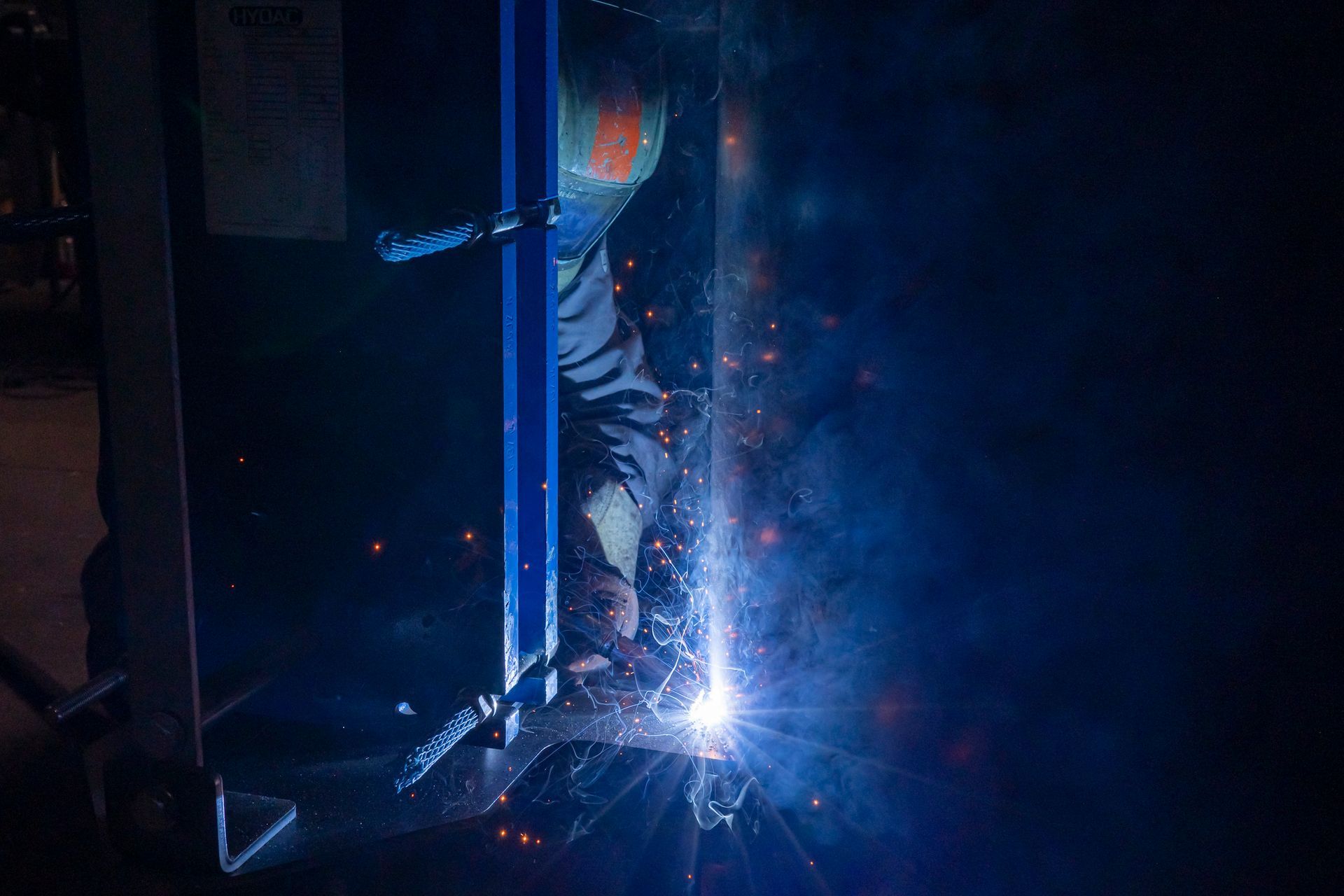 Soudeur dans un atelier sombre, des étincelles jaillissent, soudage de métal sur une poutre de support verticale.