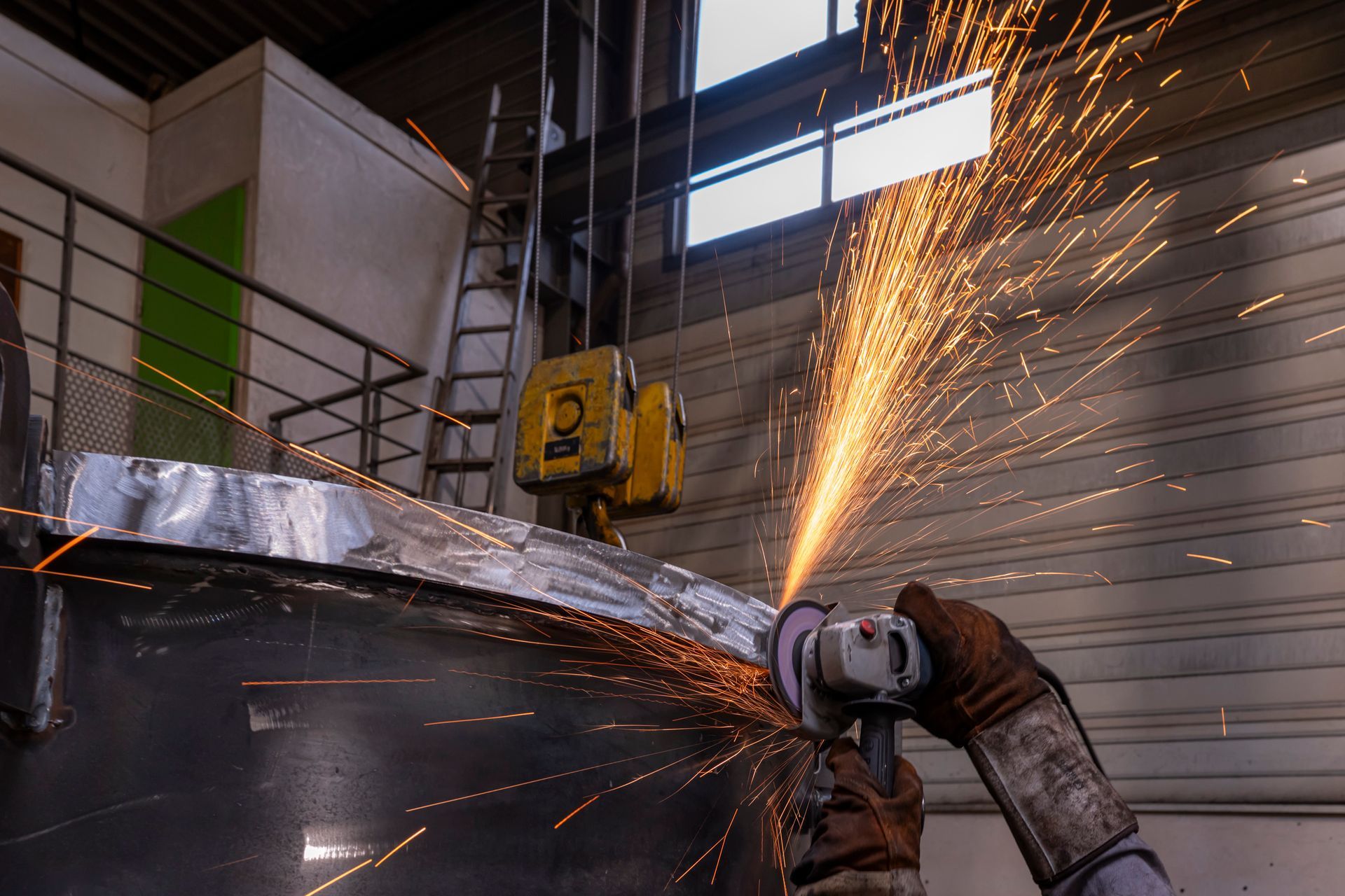 Une personne meule du métal, des étincelles jaillissent dans un atelier.