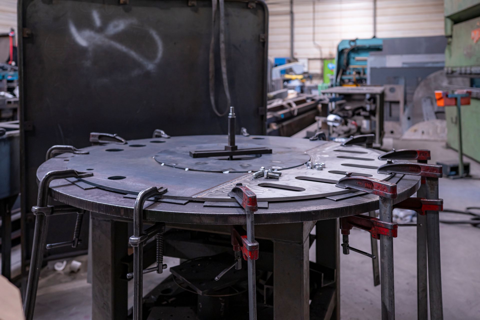 Poste de travail pour la fabrication métallique avec table circulaire, pinces et diverses pièces métalliques. Aménagement d'atelier.