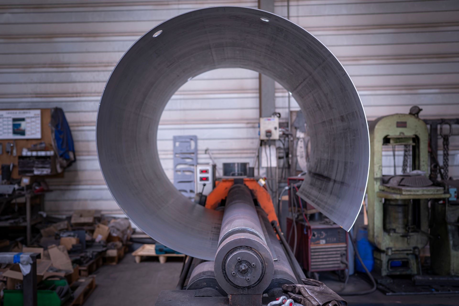 Un grand cylindre métallique est en cours de fabrication dans un atelier. Une machine à rouleaux cintre la tôle pour lui donner la forme d'un grand cercle.