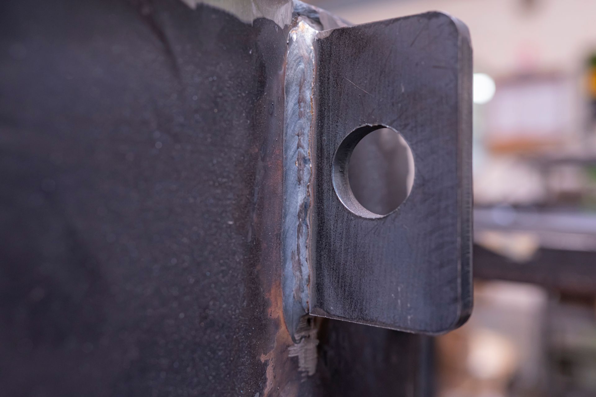 Gros plan sur un support métallique soudé avec un trou circulaire, fixé sur une surface peinte foncée.