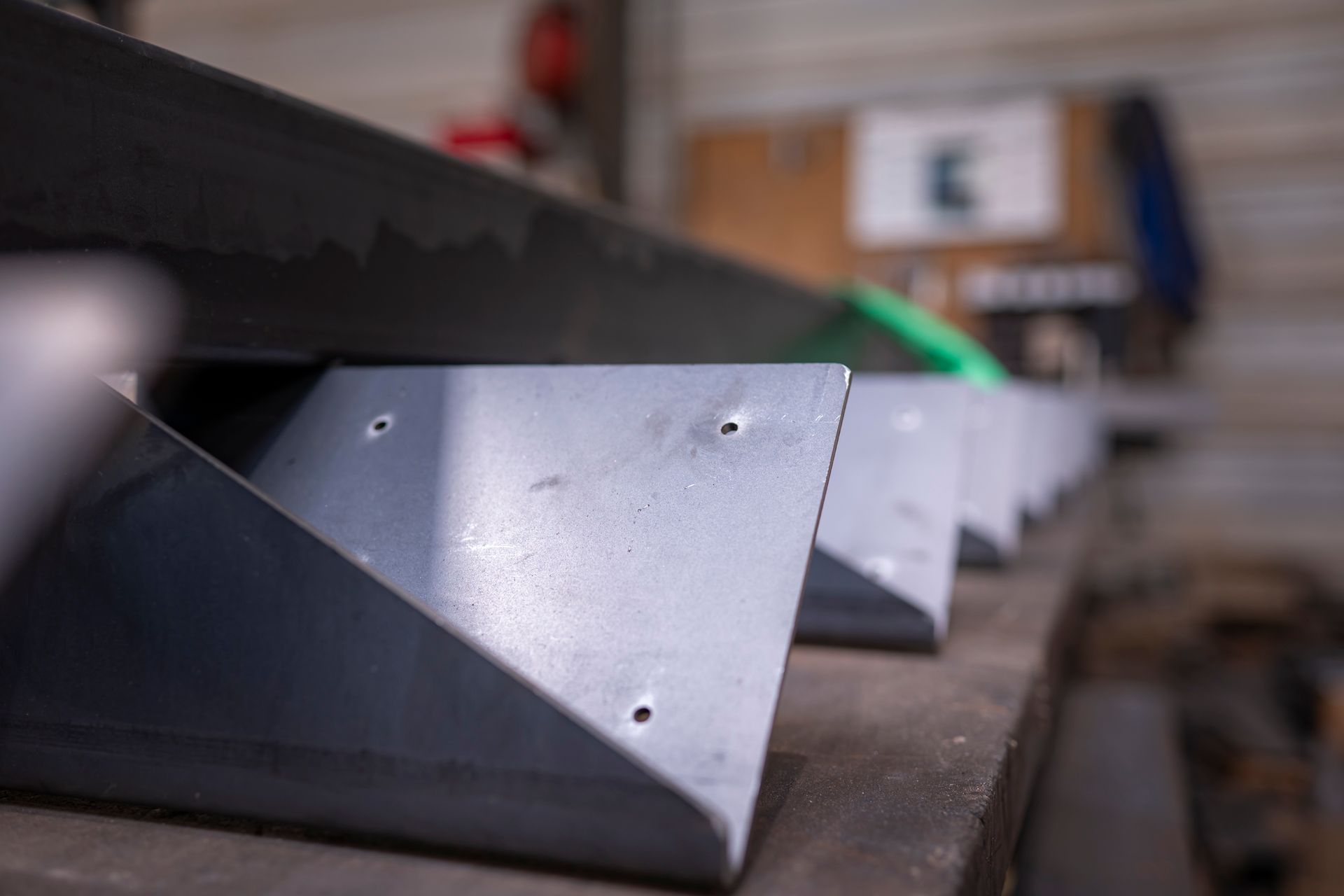 Gros plan sur des supports métalliques avec trous de fixation, alignés sur une surface dans un atelier.