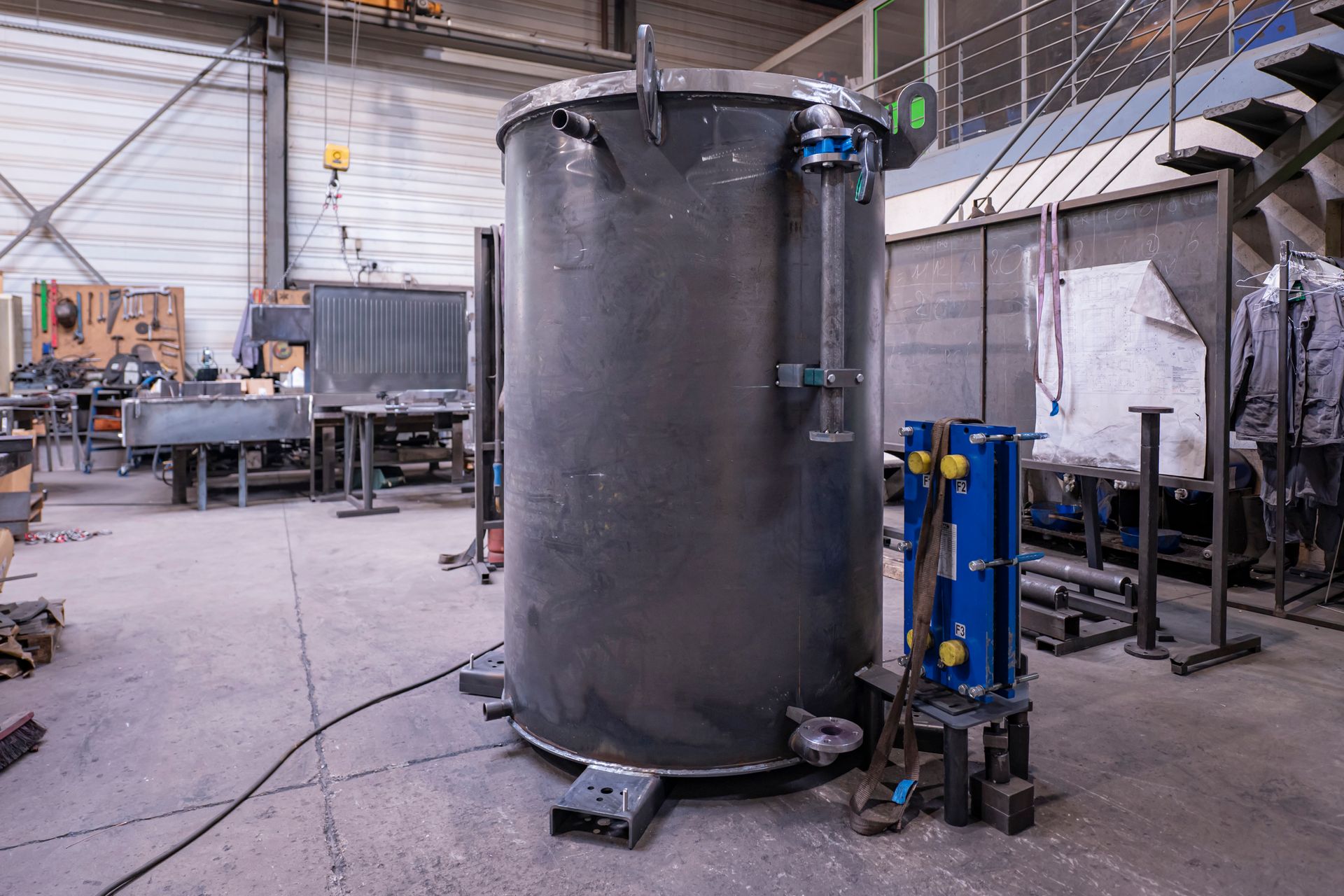 Grand réservoir cylindrique en métal avec tuyaux et manomètres intégrés, dans un environnement d'atelier.