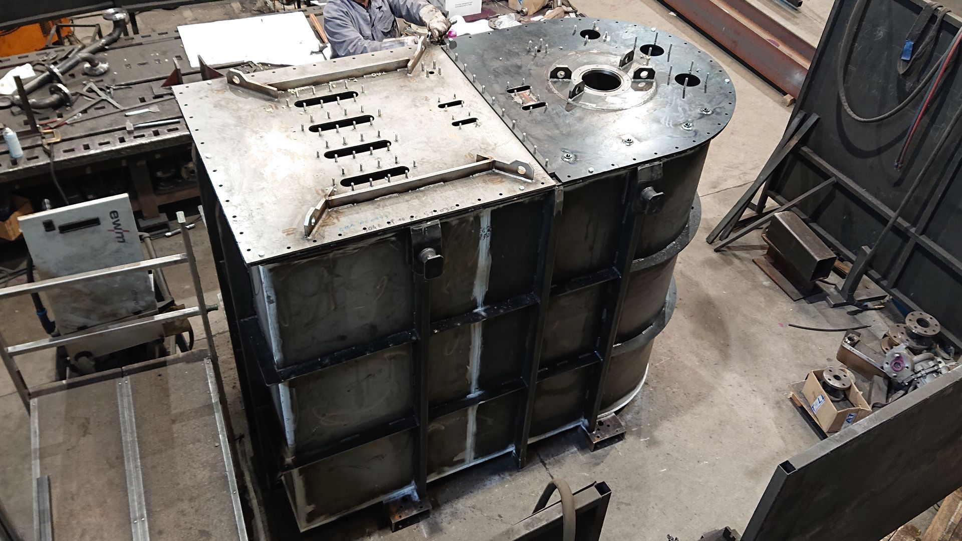 Réservoir en acier assemblé en atelier, probablement à usage industriel. Sections rectangulaires et courbes, construction soudée.