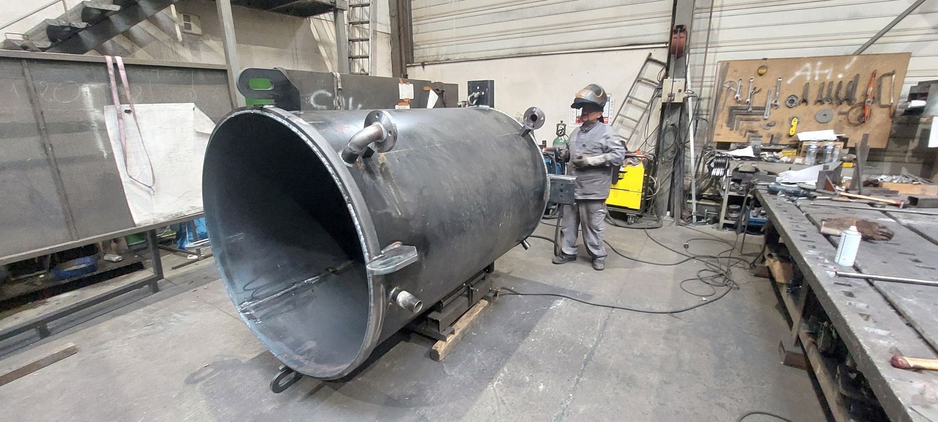 Une personne soude un grand cylindre métallique dans un atelier.