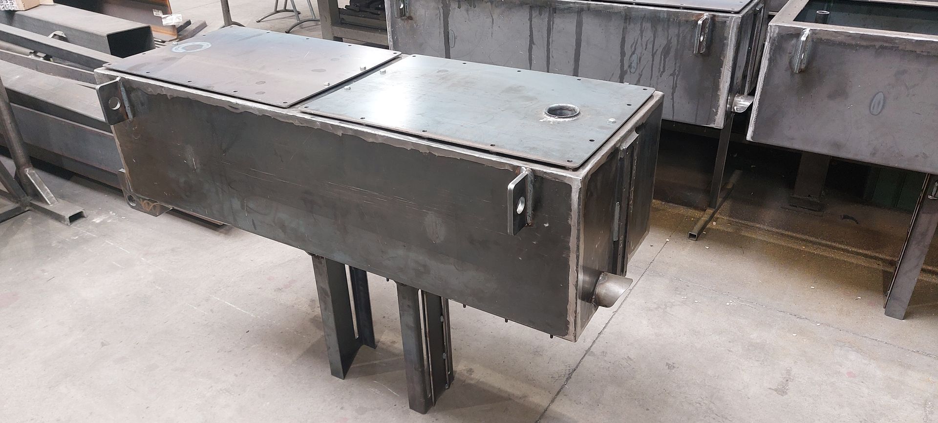 Une structure métallique rectangulaire sur pieds, avec couvercle amovible et robinet.