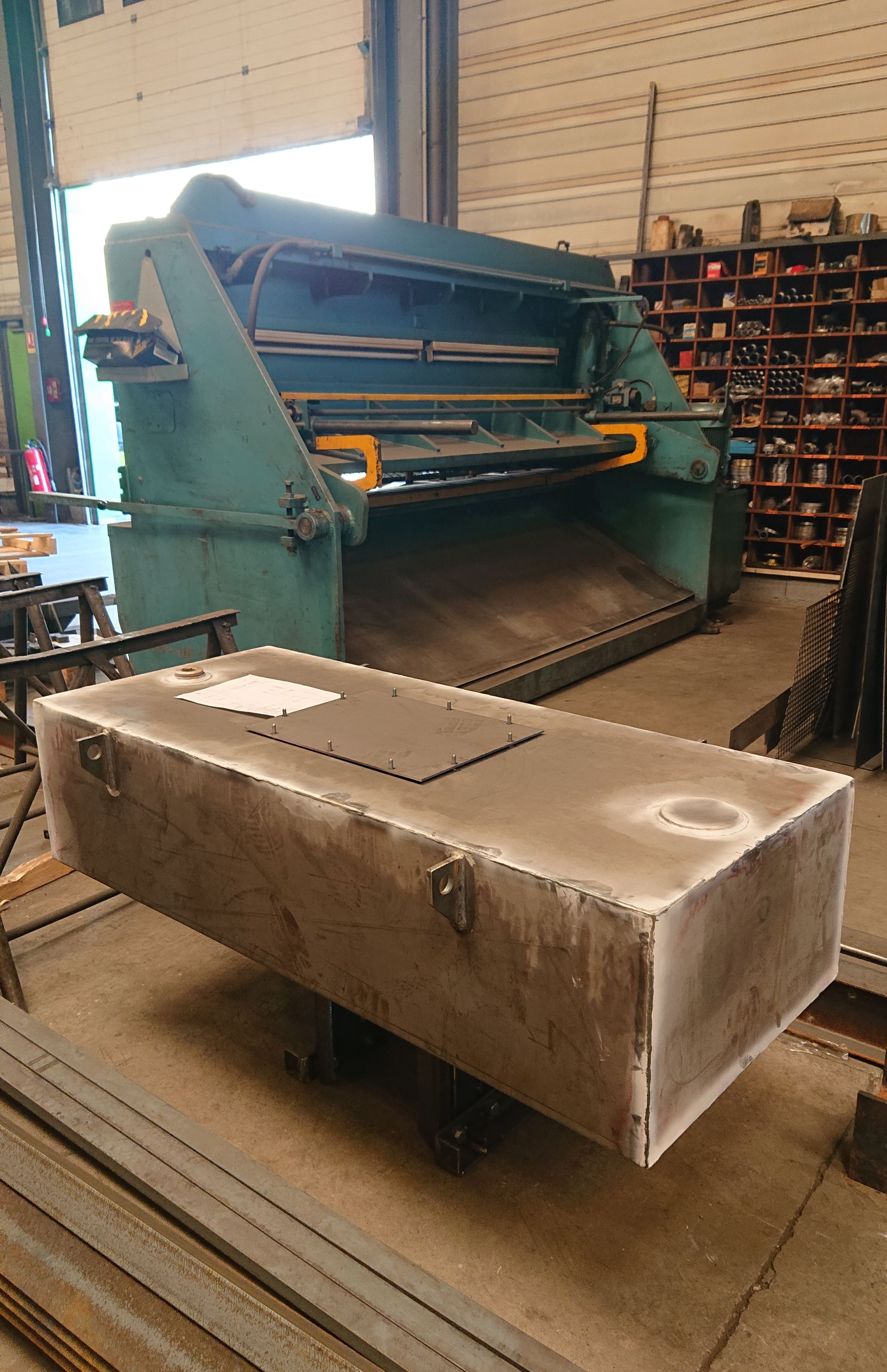 Grand réservoir dans un atelier, avec une machine derrière.