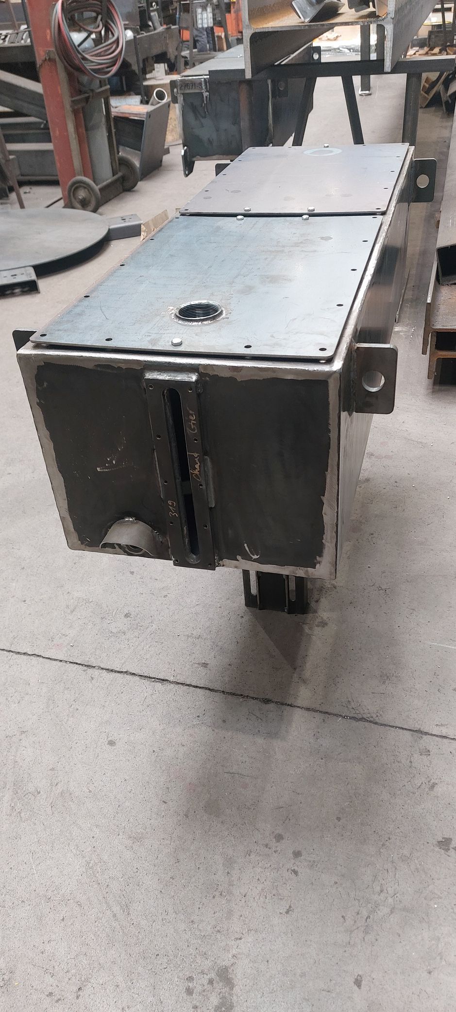 Boîte métallique avec une fente sur le devant, sur un sol en béton gris, dans un atelier.