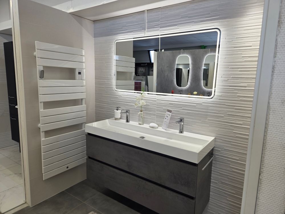 Une salle de bains avec une grande vasque qui contient deux mitigeurs et un grand miroir lumineux