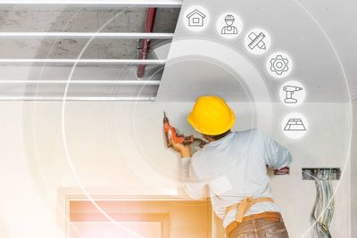 Ouvrier portant un casque jaune installant des luminaires de plafond à l'aide d'outils dans une pièce blanche
