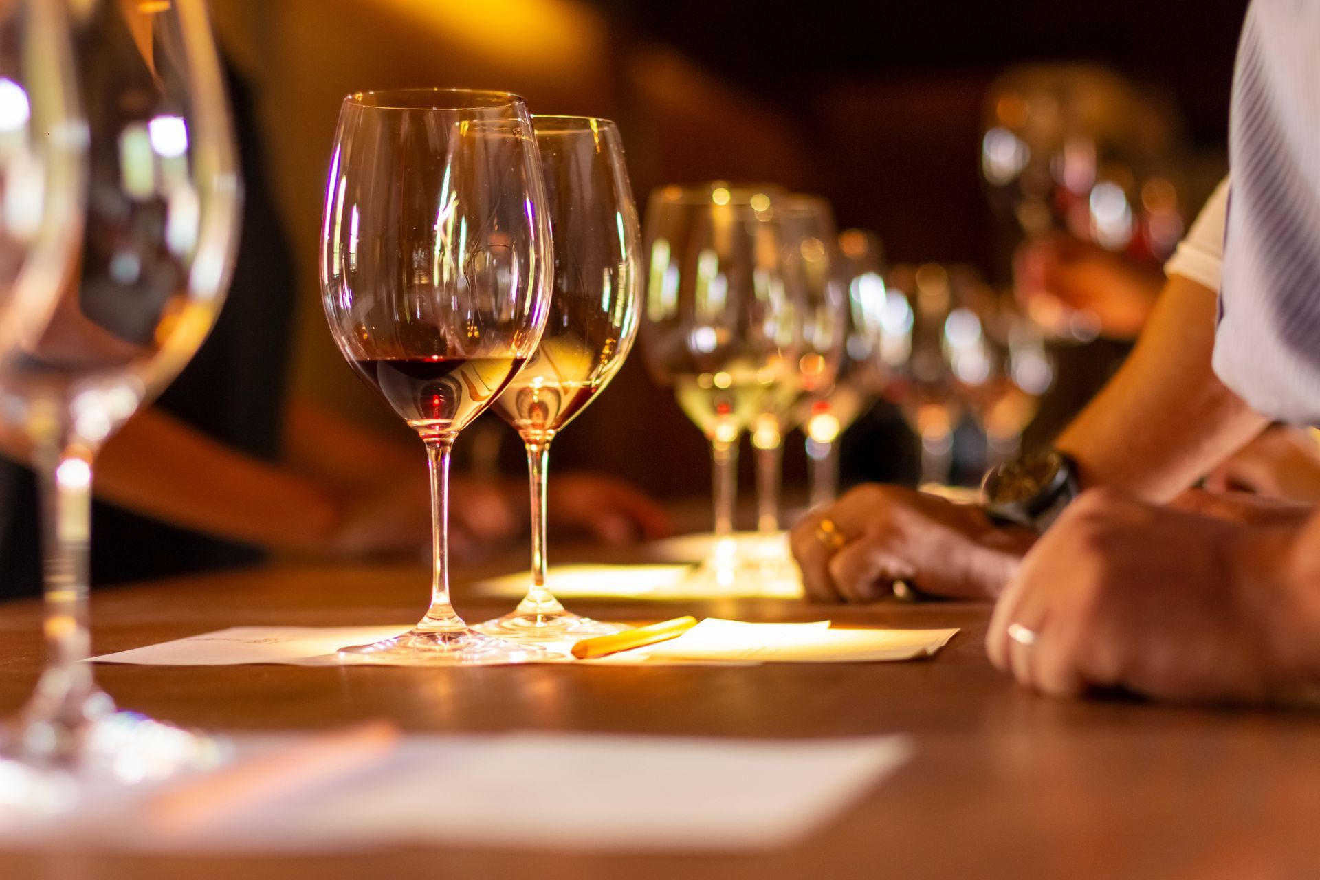 Du vin rouge est versé d'une bouteille dans un verre tenu à la main lors d'un événement social, avec plusieurs personnes en arrière-plan.