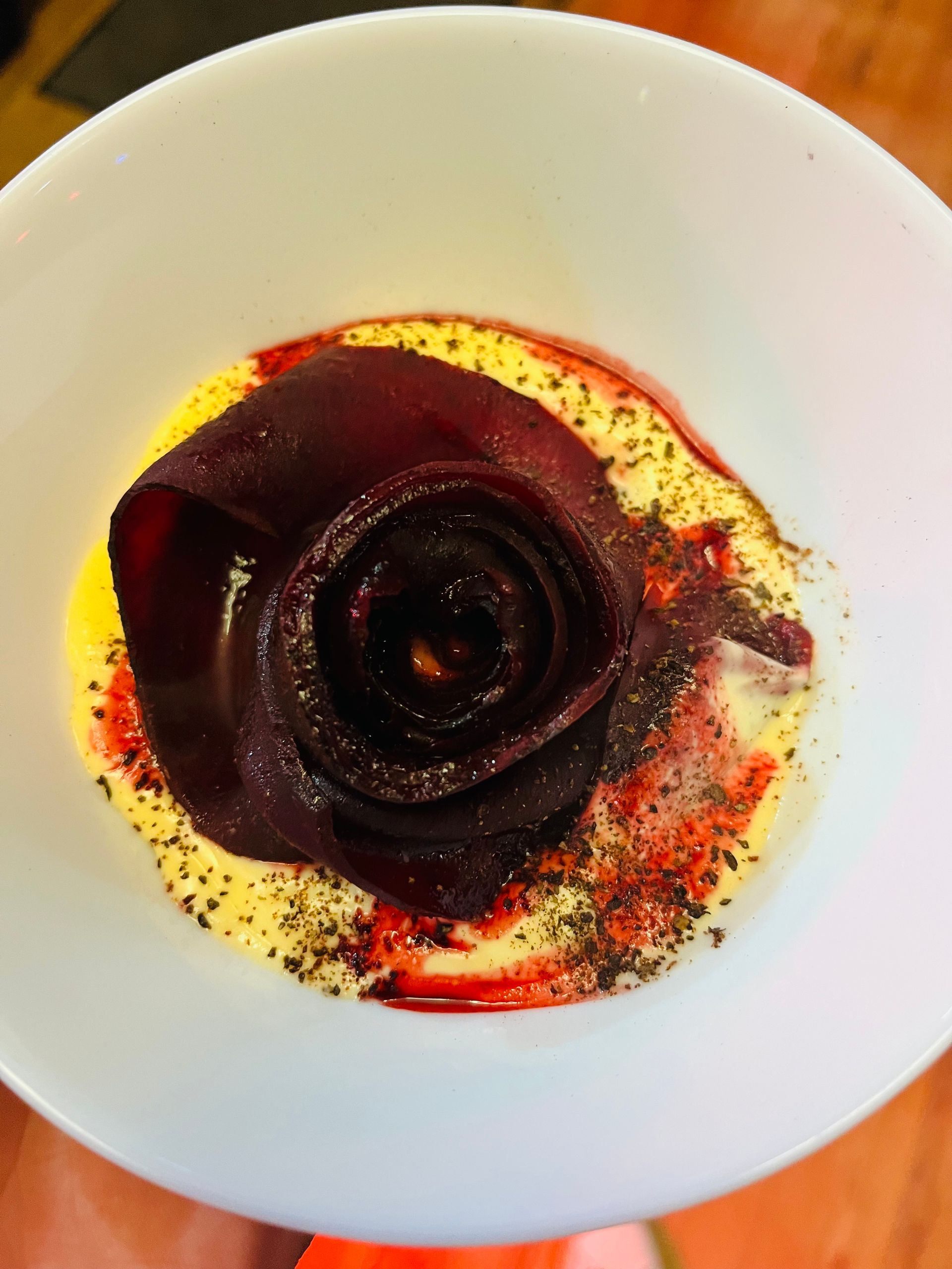 Une rose en forme de fine tranche de betterave rôtie, servie dans un bol blanc sur une sauce crémeuse et parsemée d'herbes.