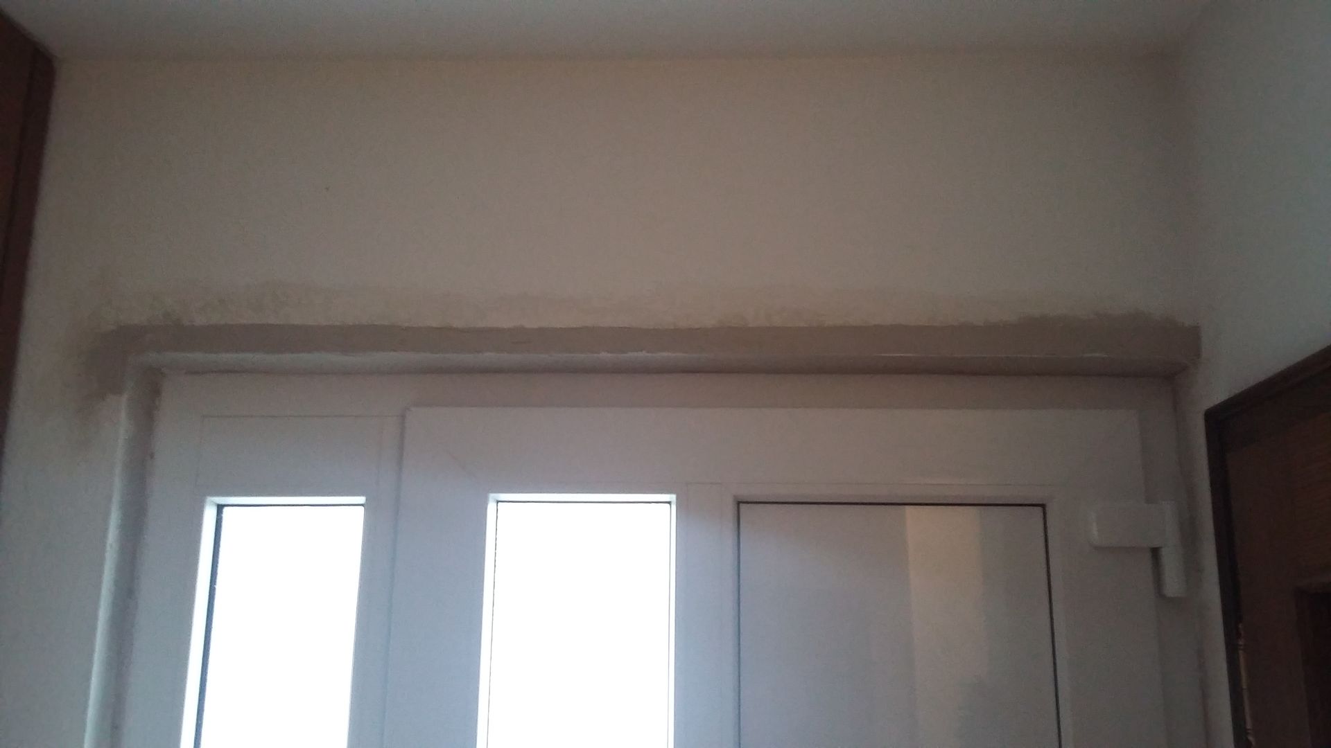 In einem Flur befindet sich eine weiße Tür mit drei Fenstern.