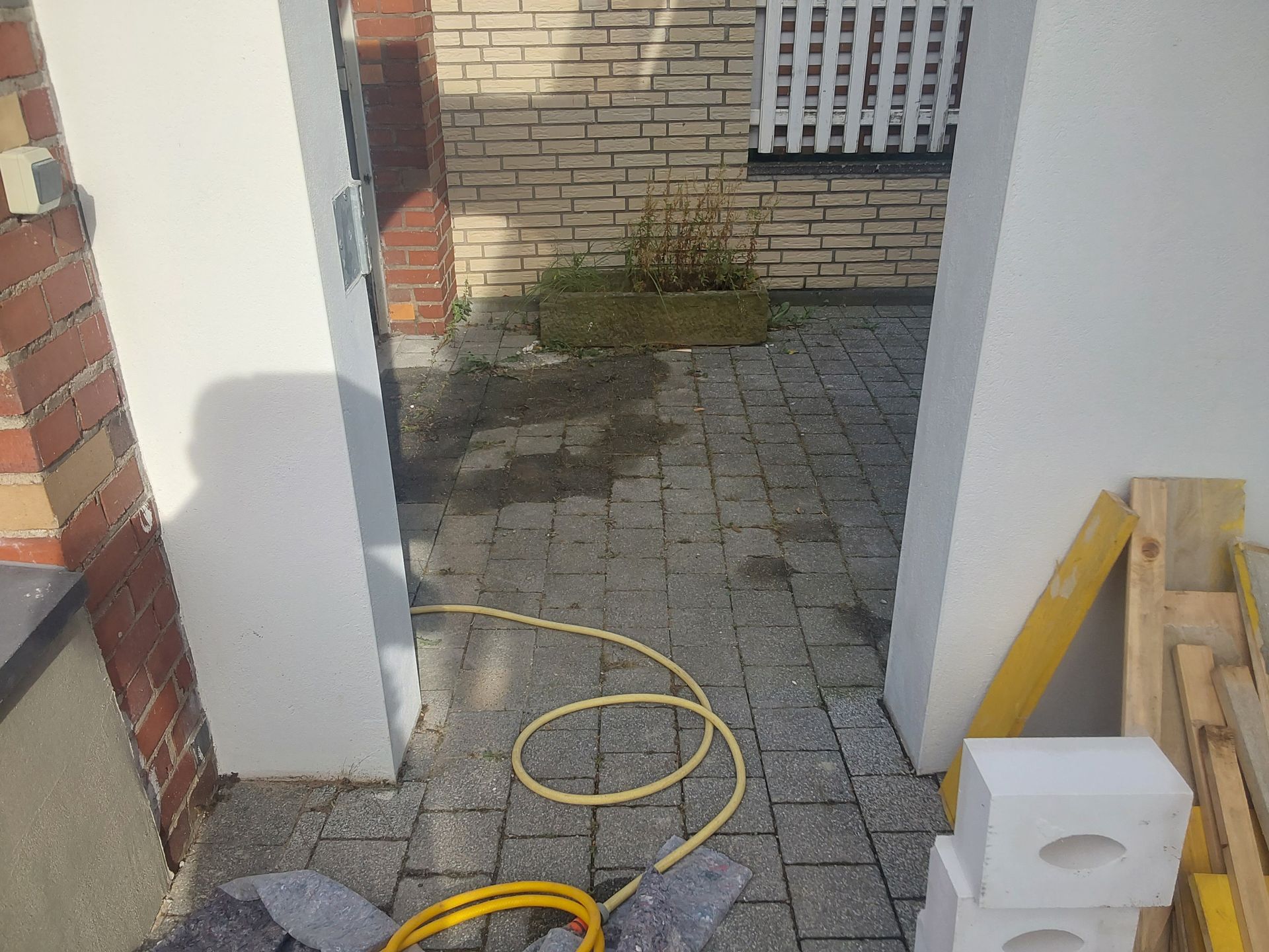 Ein gelber Schlauch liegt auf dem Boden neben einer Ziegelmauer