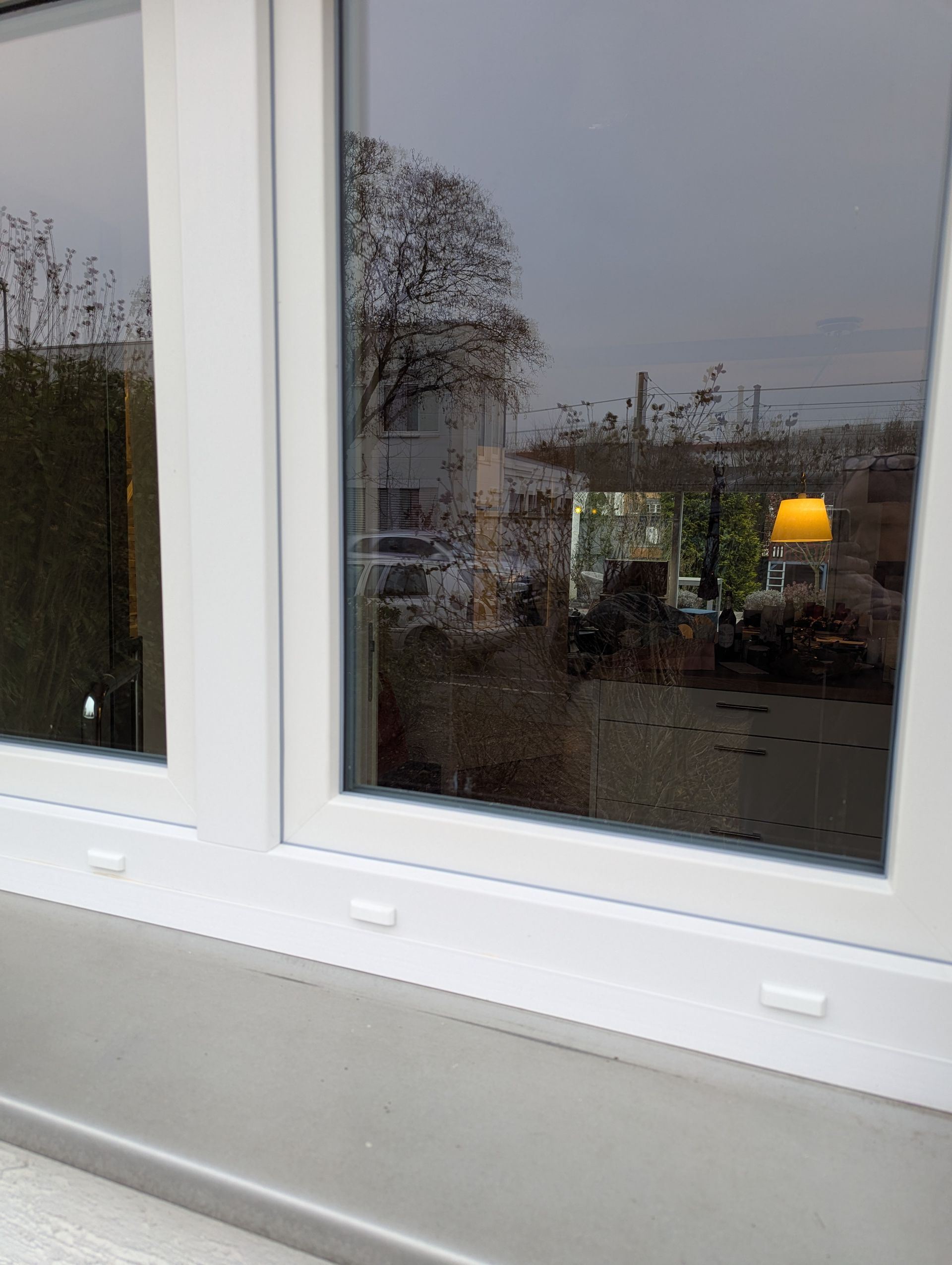 Ein weißes Fenster mit der Spiegelung einer Lampe darin.