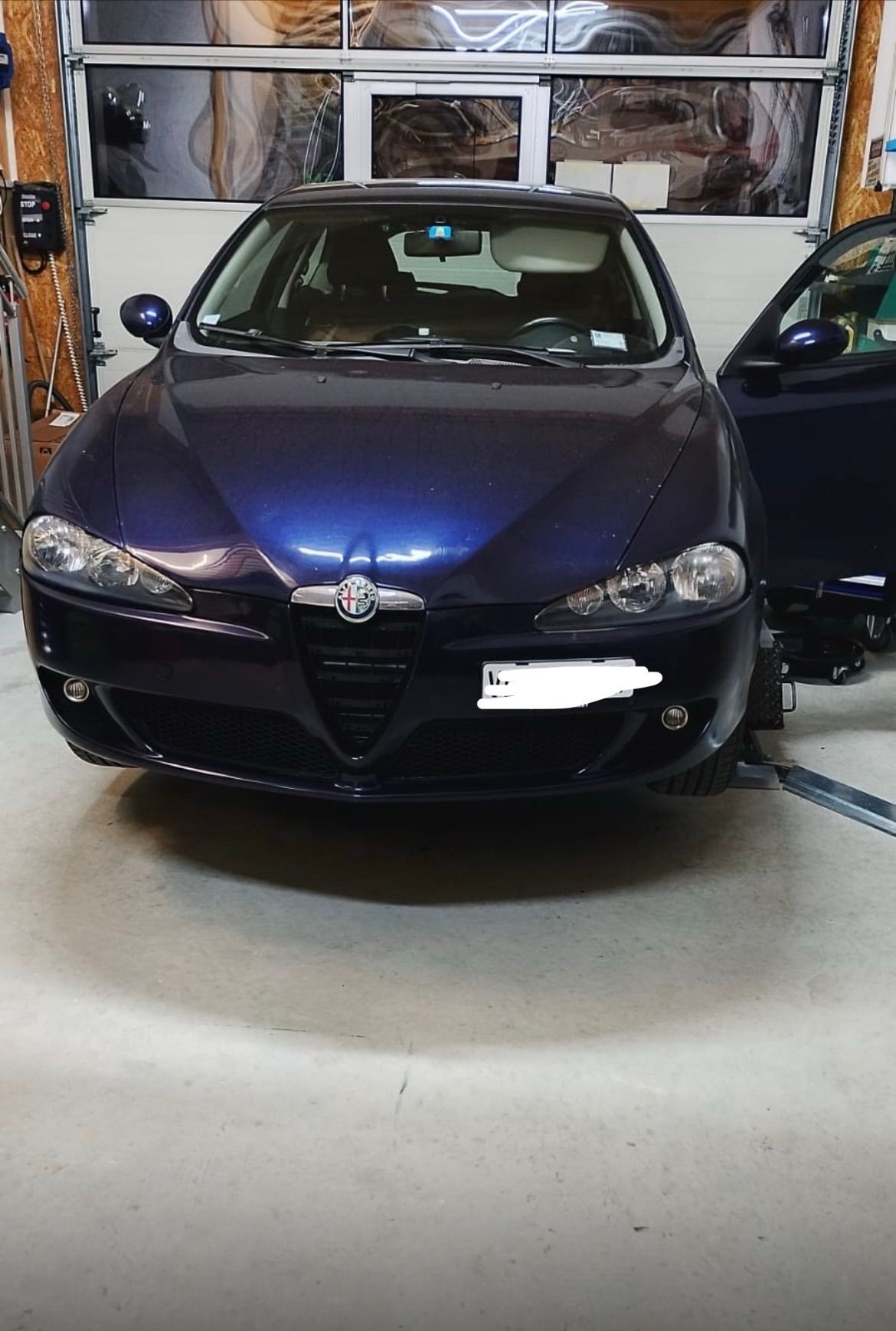 Une Alfa Romeo bleu foncé garée dans un garage, la portière côté conducteur ouverte.