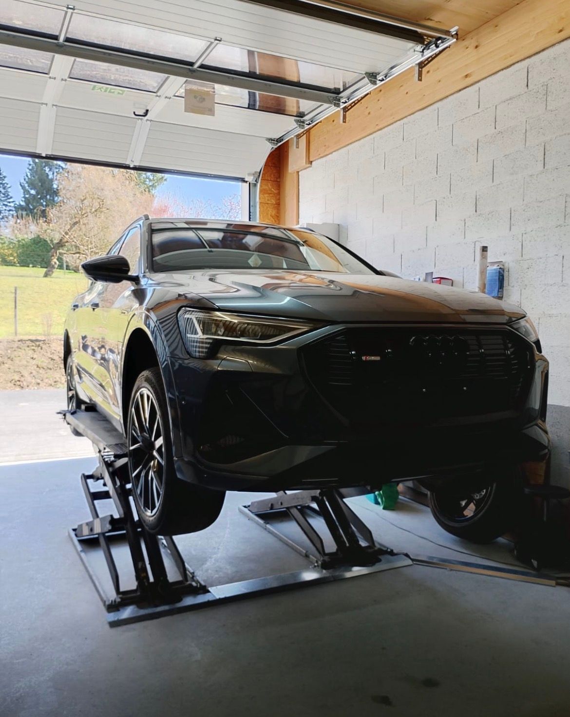 Un SUV électrique Audi gris foncé, surélevé sur un pont élévateur hydraulique à l'intérieur d'un garage bien éclairé.
