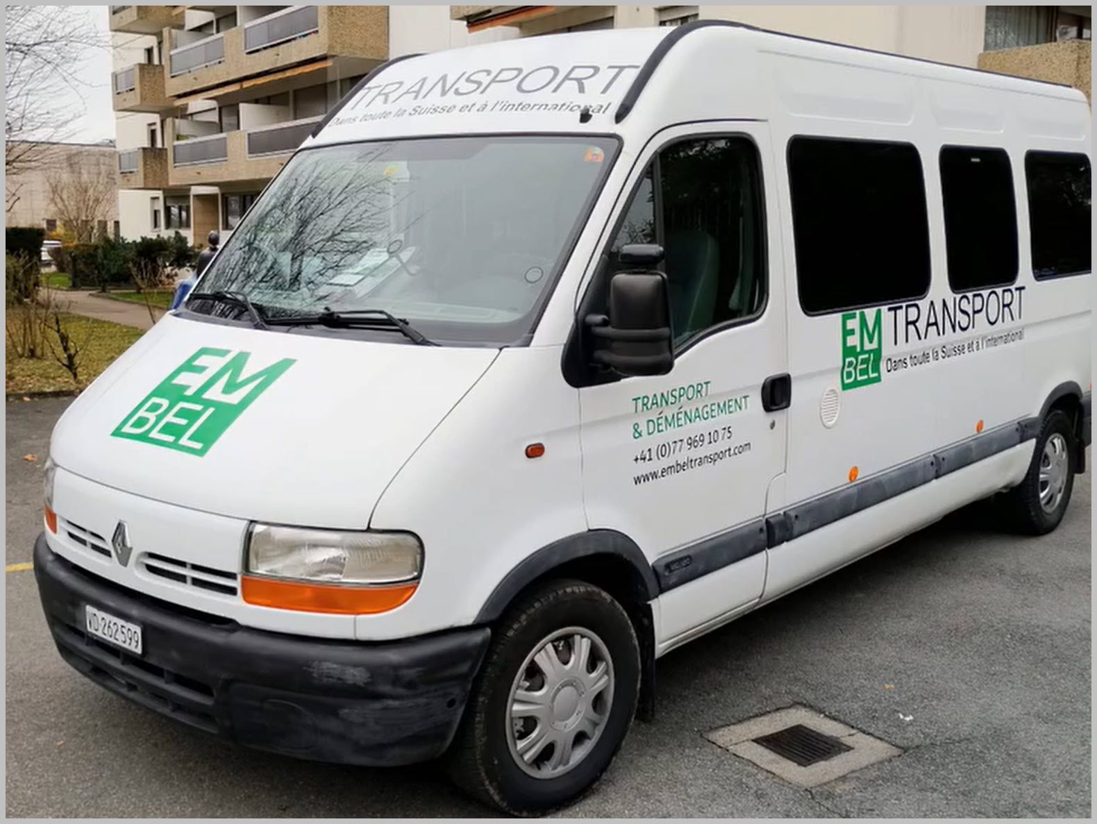 Fourgonnette de transport blanche EM BEL stationnée à l'extérieur.