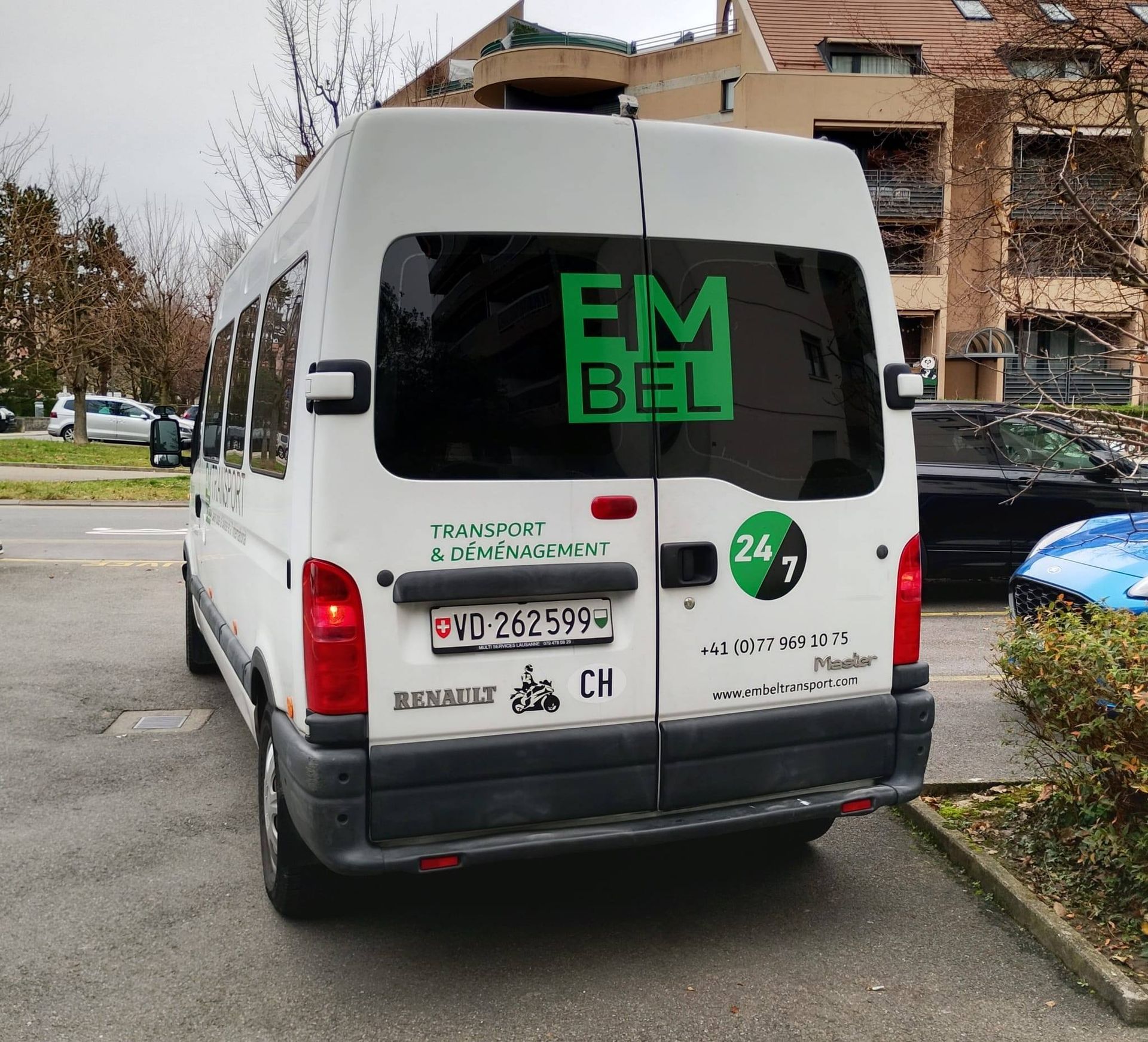 Une camionnette Renault Master blanche garée à l'extérieur, avec l'inscription « EMBEL » et un logo 24/7.