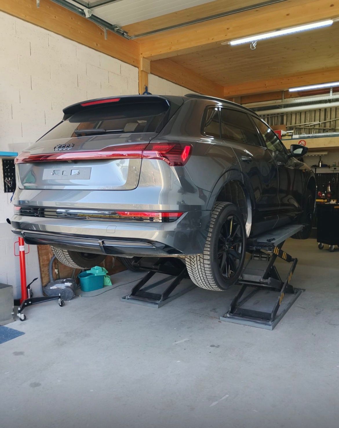 Un SUV gris sur un pont élévateur dans un garage, les roues arrière démontées et le dessous de caisse exposé.