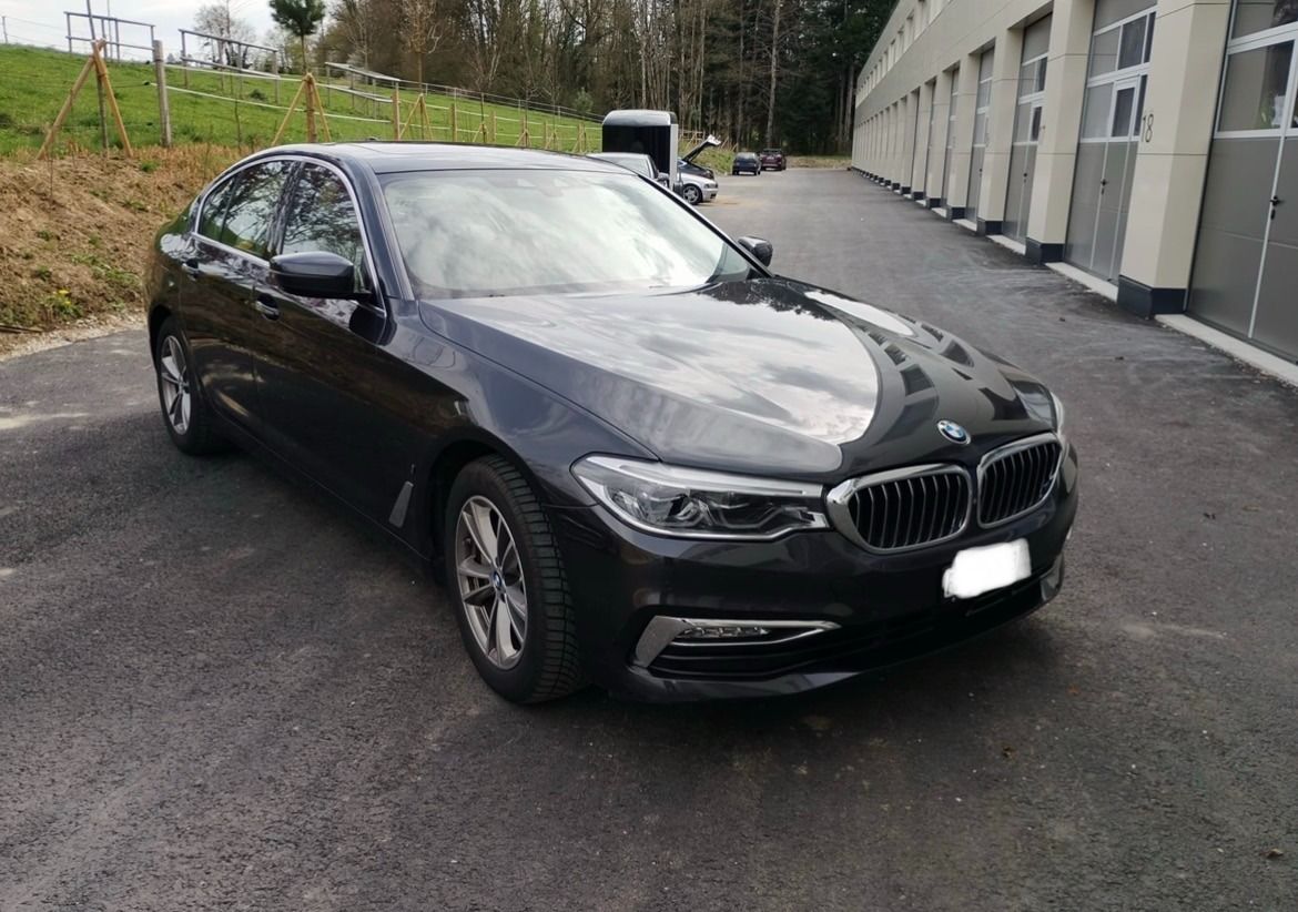 Une berline BMW noire garée sur le bord d'une route mouillée, près d'une rangée de bâtiments.