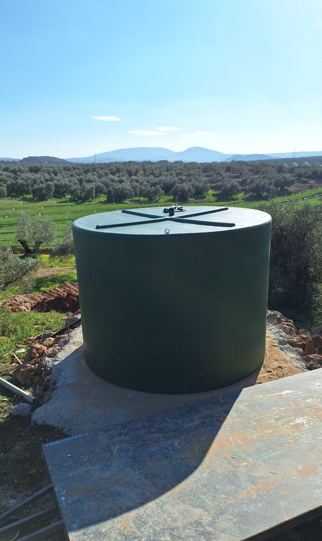 Un gran tanque verde está sentado encima de una plataforma de concreto en el medio de un campo.