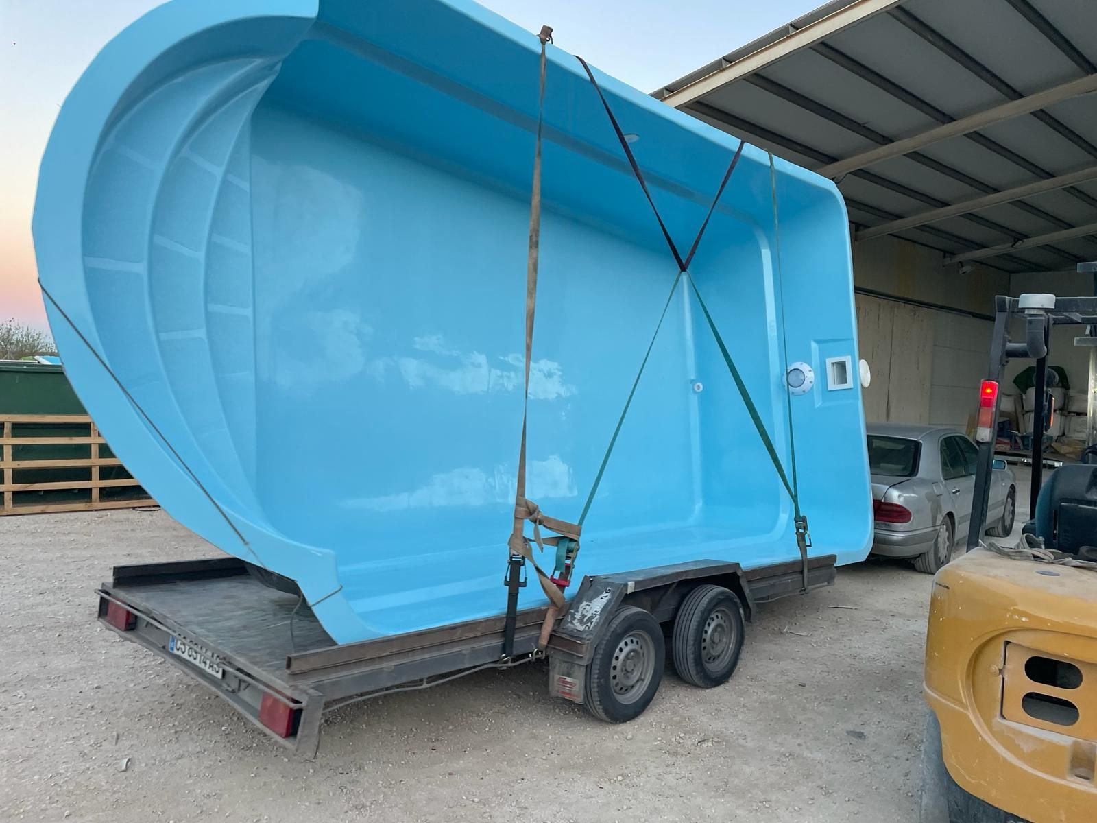 Una gran piscina azul está sobre un remolque que está siendo levantado por una carretilla elevadora.