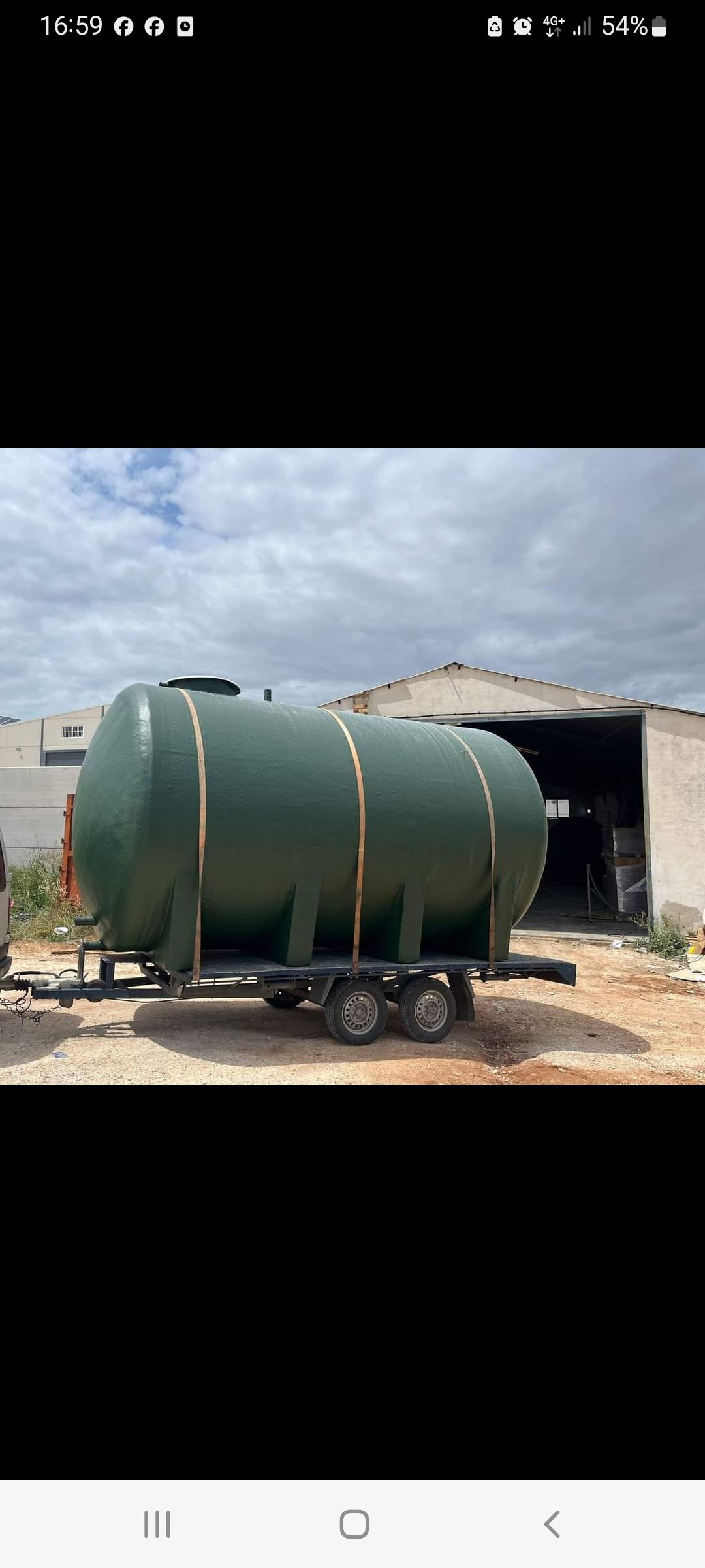 Un gran tanque verde está en un remolque frente a un edificio.