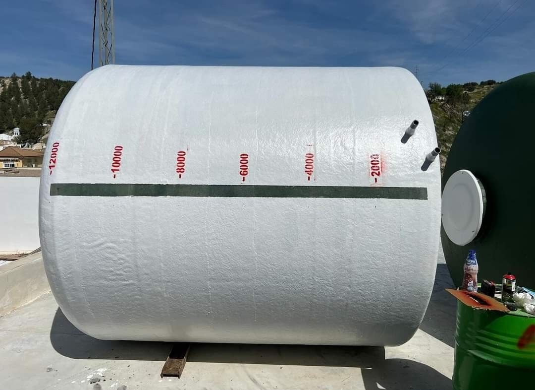 Un gran tanque blanco está sentado en el suelo al lado de un barril verde.