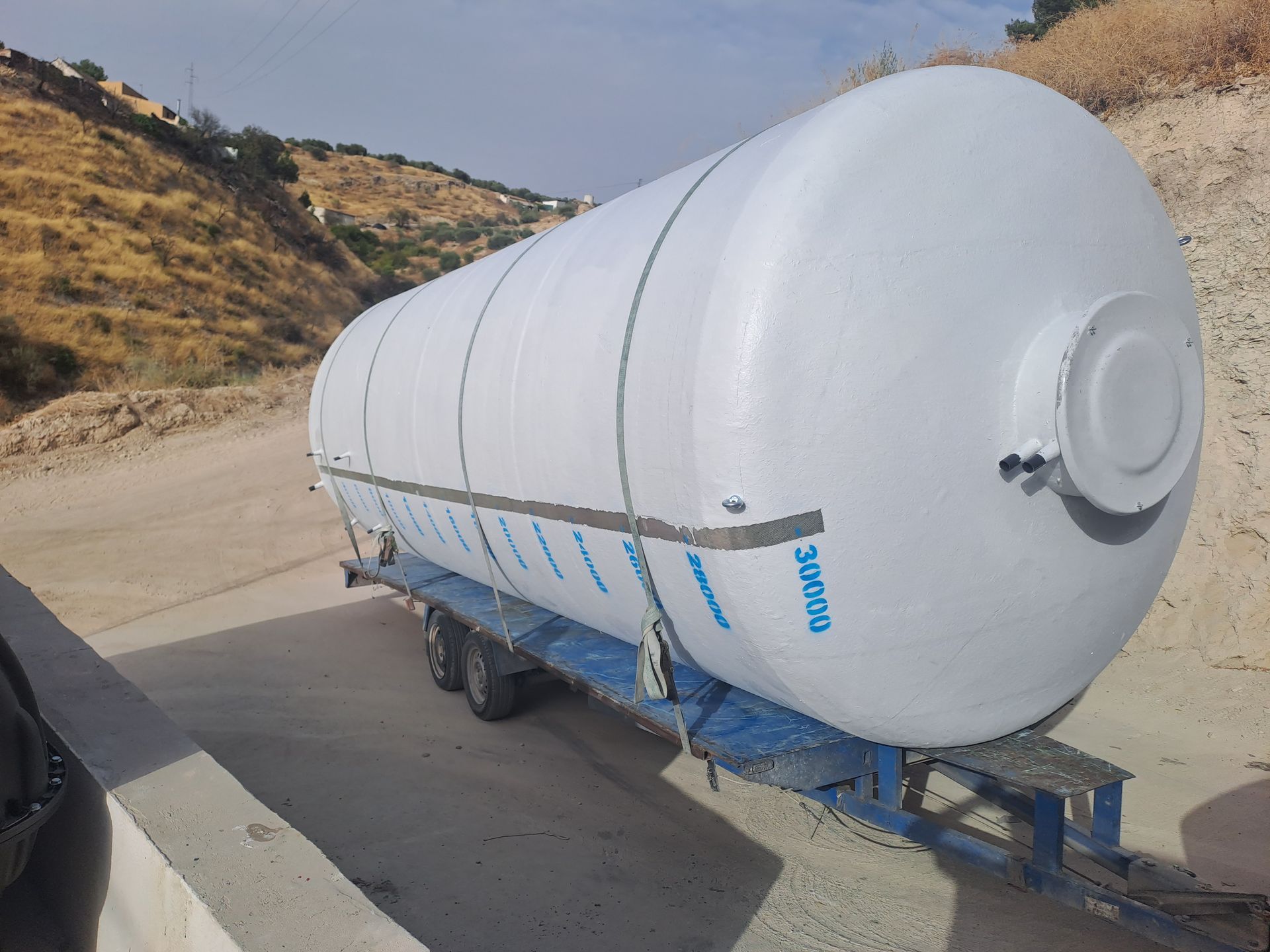 Un gran tanque blanco está sentado encima de un remolque azul.