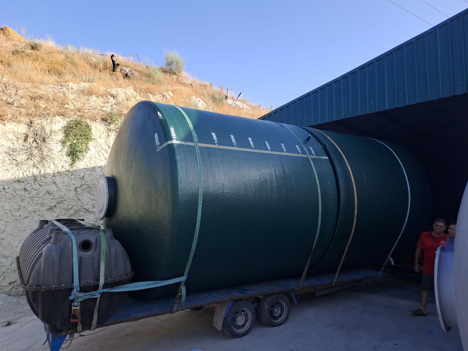 Un gran tanque verde está en un remolque frente a un edificio.