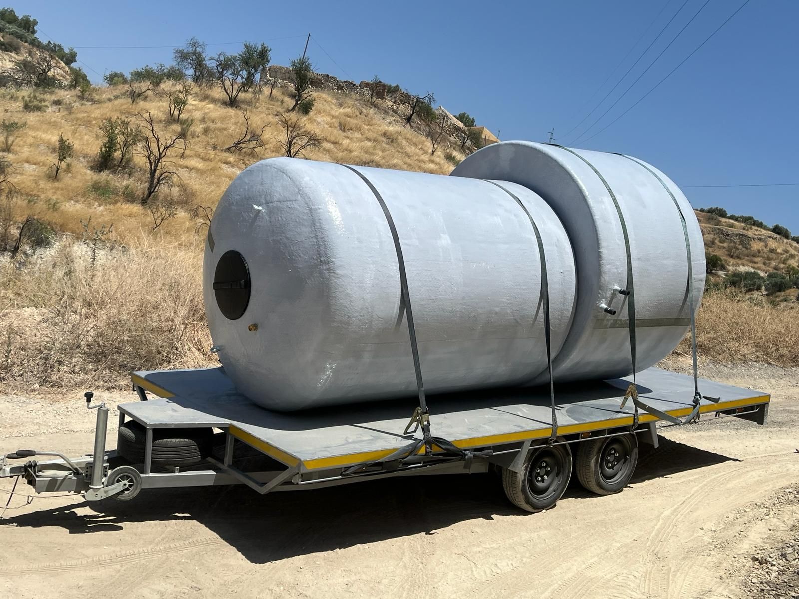 Un tanque grande está sentado encima de un remolque en un camino de tierra.