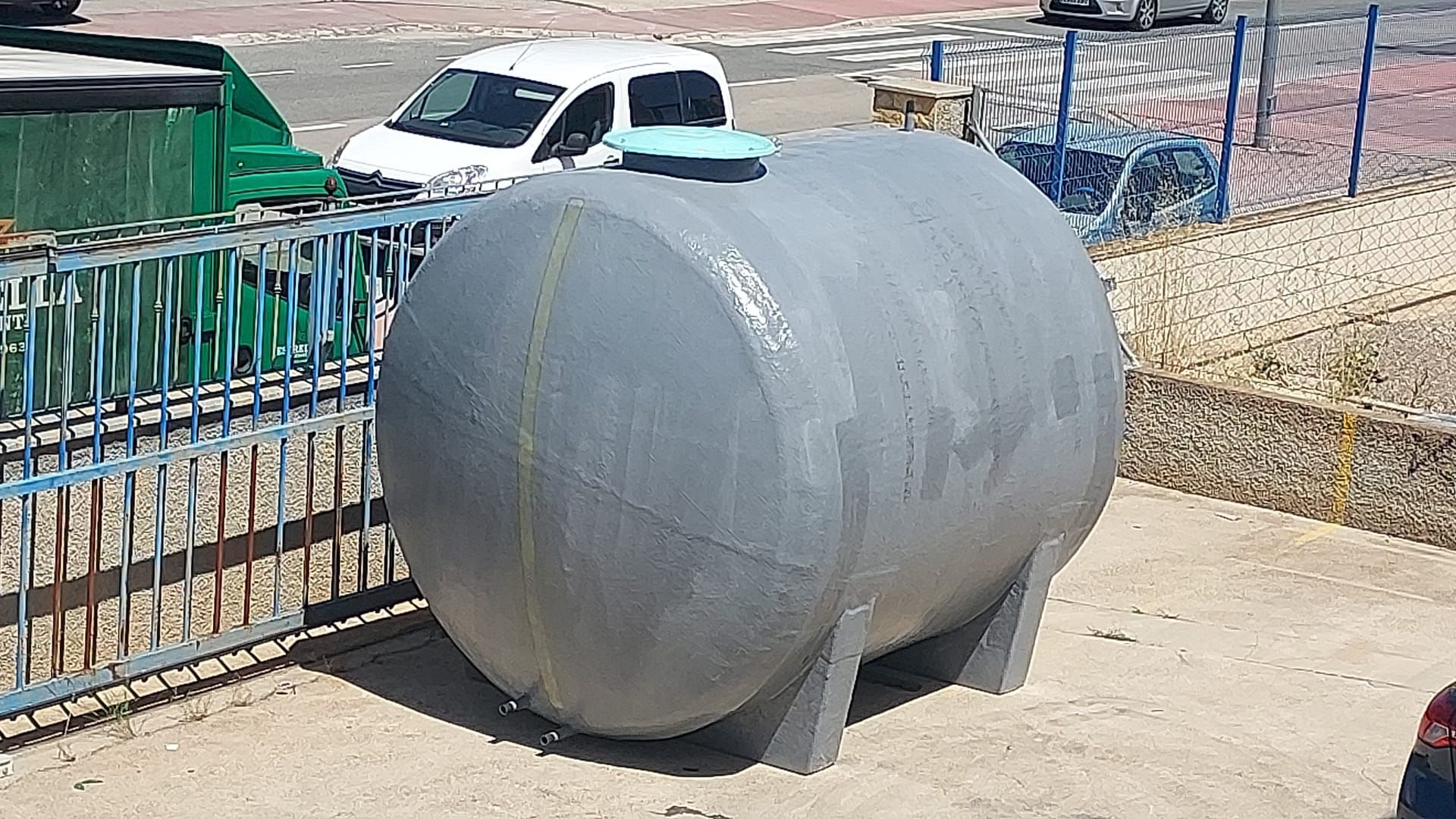 Un gran tanque gris está sentado en la tierra al lado de una valla.